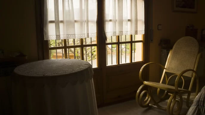 Camera semplice con tavolino coperto da tovaglia e sedia a dondolo.