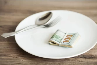 Banconote da 100 dollari arrotolate su un piatto bianco con posate.