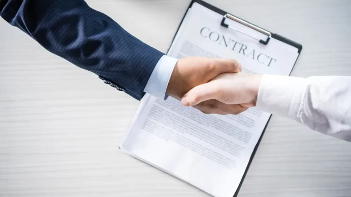 Stretta di mano tra due persone sopra un contratto, simbolo di accordo commerciale o prenotazione alberghiera.