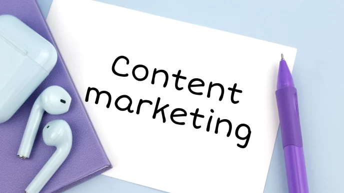 AirPods bianchi e penna viola su quaderno viola con nota 'Content marketing'