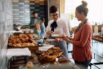Cameriera sorridente serve cibo a un ospite dell'hotel durante la colazione.