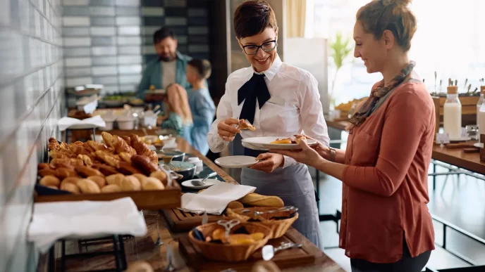 Cameriera sorridente serve cibo a un ospite dell'hotel durante la colazione.